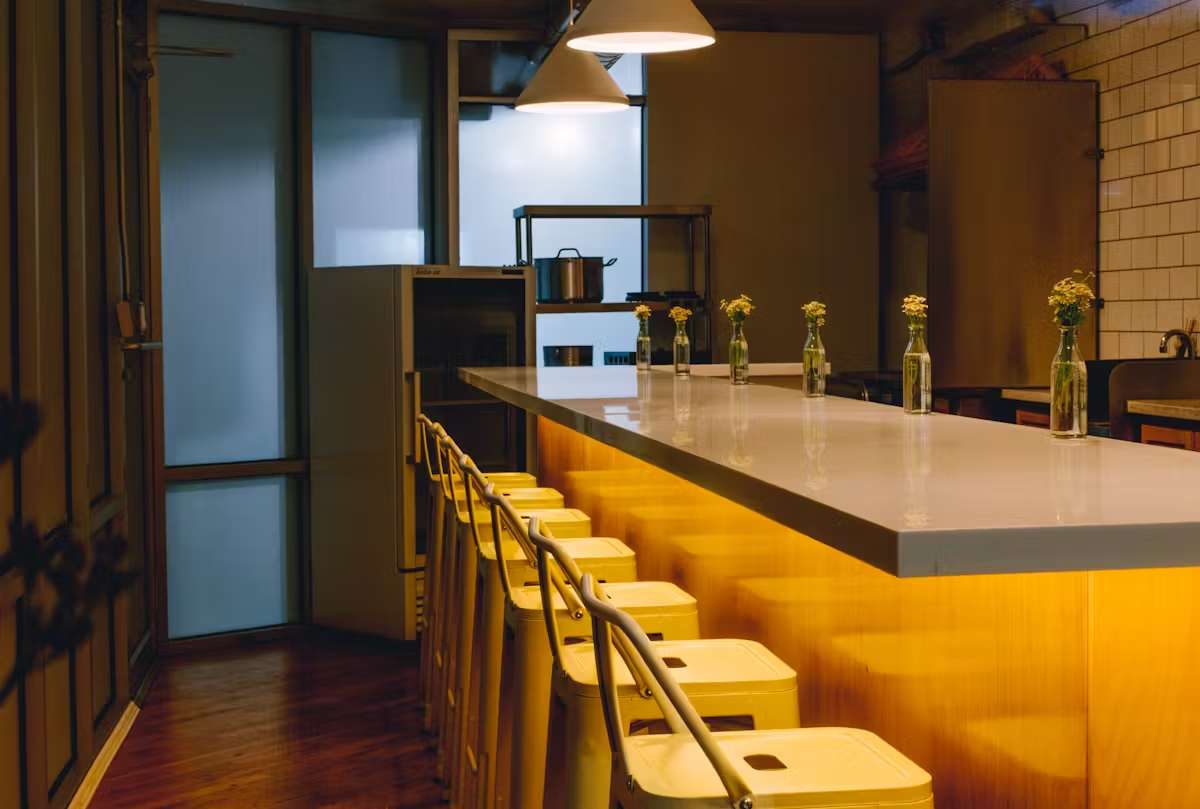 Interior view of Pearl Street Raw Bar showing the chef's counter dining area with guests seated along the kitchen watching chefs prepare modern seafood dishes